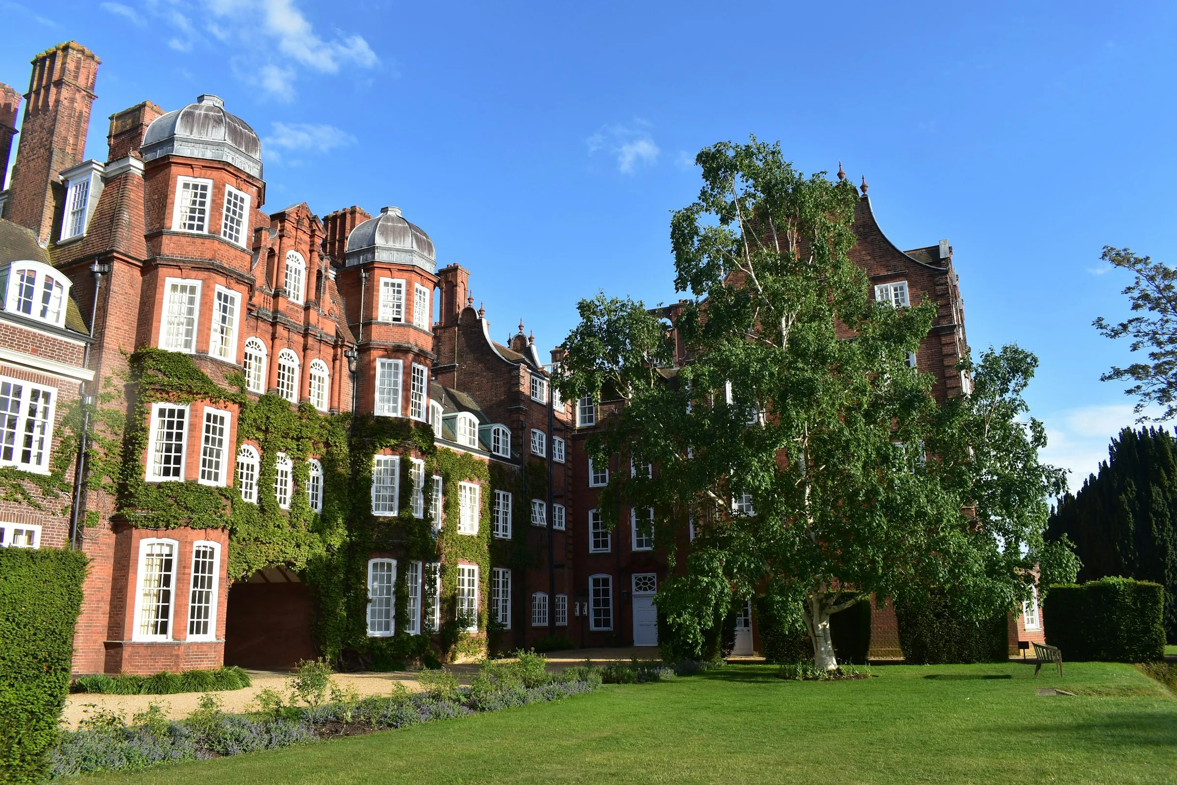A UK university campus building with ivy-covered red brick and manicured lawns